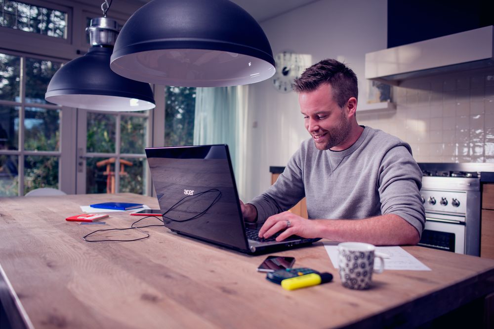 man met laptop aan de keukentafel