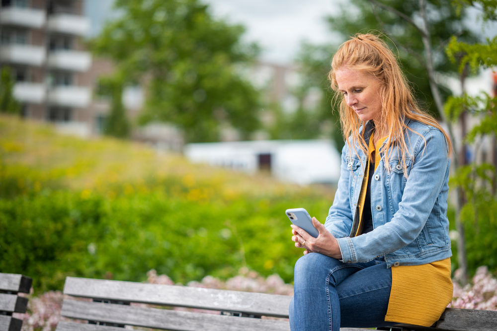 Vrouw op bankje in het park met haar telefoon