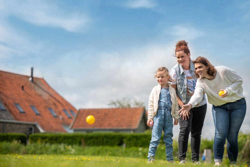 twee vrouwen en kind spelen jeu de boule op gras